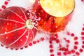 Red Christmas ball on natural white snow with square beads and burning candle in a glass candlestick. Christmas, New year outdoor Royalty Free Stock Photo