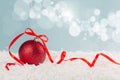 Red Christmas ball with a scarlet satin bow in the snow on a blue background with bokeh lights. happy new year card Royalty Free Stock Photo