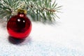A red Christmas ball and a snow-covered Christmas tree branch on a snowy white background with a place for copyspace text. New Royalty Free Stock Photo
