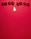 Red christmas balls on thread and in the middle is a wooden Christmas tree with glitters on the tips on the top side on red Royalty Free Stock Photo