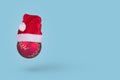 Red Christmas bauble ball ornament with Santa Claus hat flying in air isolated on  pasel blue background Royalty Free Stock Photo