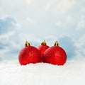 Red Christmas baubles on white snow background against blue sky with white clouds. Winter holidays concept Royalty Free Stock Photo