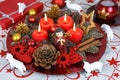 Red Christmas decorated wreath plate with four burning candles on a table cloth surrounded with white sheep