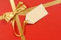 Red Christmas gift background, gold ribbon bow, blank manila gift tag or label