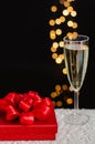 Red christmas gift box with blurred focus of a glass of sparkling wine Royalty Free Stock Photo