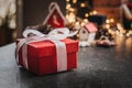 A red Christmas gift box with a white ribbon lies on the table against a bokeh background Royalty Free Stock Photo