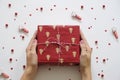 Red christmas gift in woman`s handson white background and decorations, flat lay