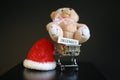 Red Christmas hat, coins in miniature of trolley and cute teddy bear toy isolated on black dark background Royalty Free Stock Photo