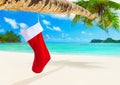 Red Christmas sock with gifts on palm tree at tropical beach. Royalty Free Stock Photo