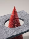 Red Christmas tree ornament piercing through circular hole in the textile base.