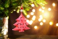 Red Christmas tree toy on a branch of a natural fir tree with lights of garlands in defocus in the background. Metal toy with Royalty Free Stock Photo