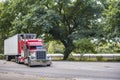 Red classic big rig semi truck with lot of polished chrome accessories and loaded refrigerator semi trailer standing on the rest Royalty Free Stock Photo