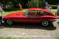 Red classic Jaguar E-Type parked on a cobblestone road surrounded by people