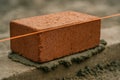 Red clay brick being precisely placed on fresh mortar for wall construction with alignment string in focus at the construction Royalty Free Stock Photo