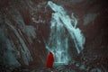 Red cloaked person looking a waterfall