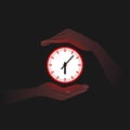 Red clock and person`s hands near it in darkness