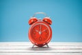 Red clock on the wooden table with blue background.