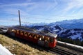 Red cogwheel train on the railway between mountain Rigi and village Vitznau in winter.