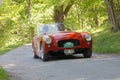 Red color Allard Palm Beach classic car from 1953 driving on a country road