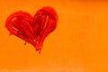 Red colored heart manually painted with drips in an orange wall