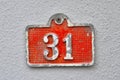 A red colored house number plaque, showing the number thirty one