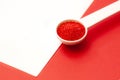 Red colored sugar in white spoon on red background - red crystals edble decor