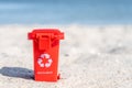 Red colored trash can recyclables with paper, plastic, glass and organic waste suitable for recycling on sandy beach. Segregate