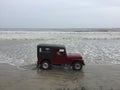 A red colour jeep being driven through a beach at Kunoor