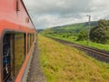 Red coloured train running through the mountain ranges of Sahyadri with mountains and cloudy sky in the background. Royalty Free Stock Photo