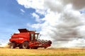 Red combine harvester is working during harvest time in the farmerÃ¢â¬â¢s fields, machine is cutting grain plants Royalty Free Stock Photo