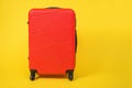 Red comfortable roomy suitcase on wheels with handle for travel stands on yellow background, front view, copy space for