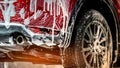 Red compact SUV car with sport and modern design washing with soap. Car covered with white foam. Car care service business concept Royalty Free Stock Photo