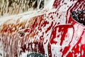 Red compact SUV car with sport and modern design washing with soap. Car covered with white foam. Car care service business concept Royalty Free Stock Photo