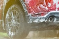 Red compact SUV car with sport and modern design washing with soap. Car covered with white foam. Car care service business concept Royalty Free Stock Photo