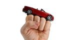 Red convertible cabriolet car model placed on raised fist of adult man, white background