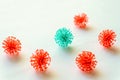 Red coronavirus balls surrounded a turquoise ball on a white flat surface