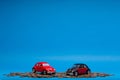 Red and a crimson car figurine placed both on top of a small pile of coins, on blue background Royalty Free Stock Photo