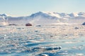 Red cruise steamboat drifting afar among the icebergs with huge rock and glacier in background, Neco bay, Antarctica