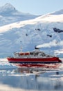 Red cruise steamboat drifting among the icebergs with huge rock and glacier in background, Neco bay, Antarctica