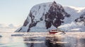 Red cruise steamboat drifting among the icebergs with huge rock and glacier in background, Neco bay, Antarctica