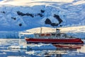 Red cruise steamboat among the icebergs with glacier in background, Neco bay, Antarctica