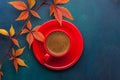 Red cup of black coffee and branch of colorful autumn leaves Virginia creeper on a dark blue-green wooden table. Flat lay