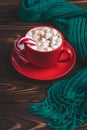 Red cup of cocoa with marshmallows and candy cane. Hot chocolate and warm knitted scarf on a dark wooden table. Winter season, Royalty Free Stock Photo