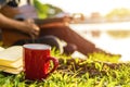 Red cup of coffee on the ground near note book and people play guitar back