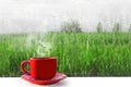 Red Cup of hot coffee on the table. The view from the window on nature. Wet fog on the window after rain.