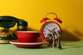 Red cup with saucer, alarm clock, vintage telephone and chessmen on light green table against yellow background Royalty Free Stock Photo