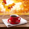 Red cup of tasty coffee on napkin, on wooden table. Autumn background