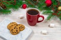 Red cup with tea, coffee with cookies and marshmallows on a white wooden table against the background of a New Year tree Royalty Free Stock Photo