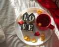 Red cup of tea with kumquat on the plate and two hearts cookies with the word LOVE on a white bed. Valentines day concept.