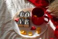 Red cup of tea with kumquat on the plate and two hearts cookies with the word LOVE on a white bed. Valentines day concept.